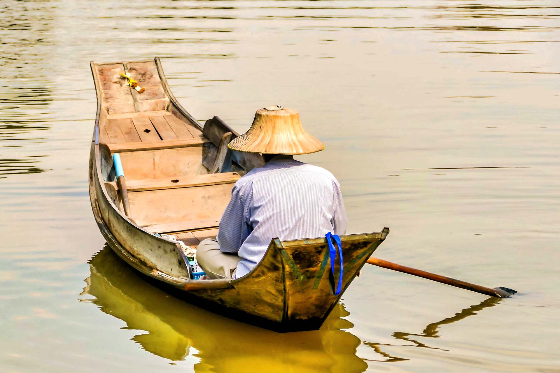 Fisherman in an Asian cone hat sailing in the lake with a small wooden boat